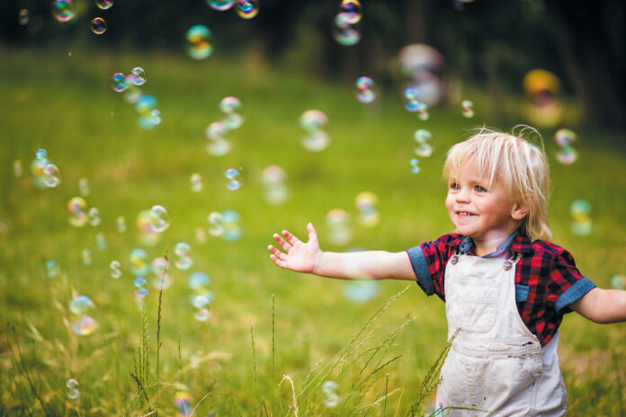 Cheerful toddler boy playing with soap bubbles in park